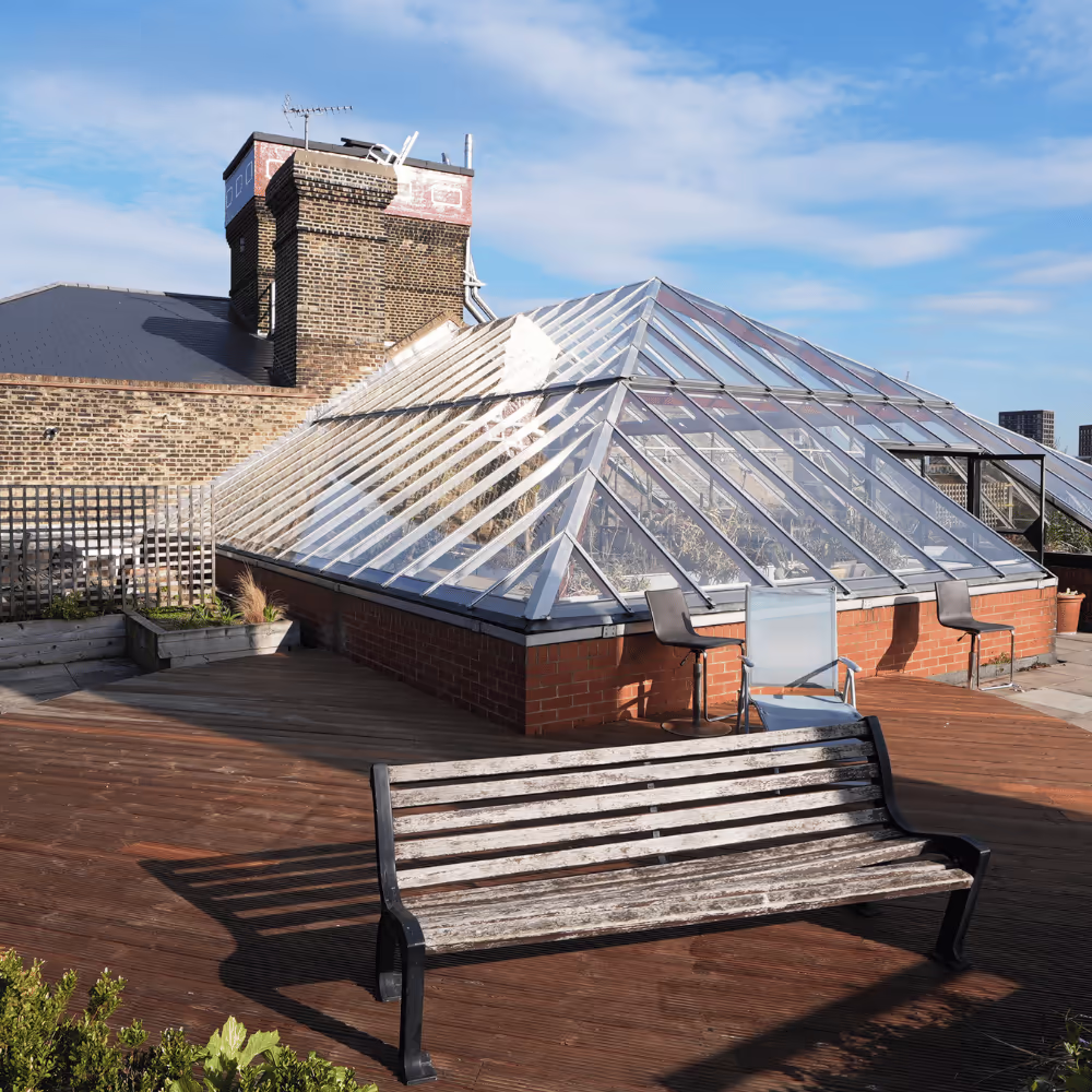 The upgraded rooftop terrace of the residential building, featuring a large glass atrium, wooden decking, and seating with a view.