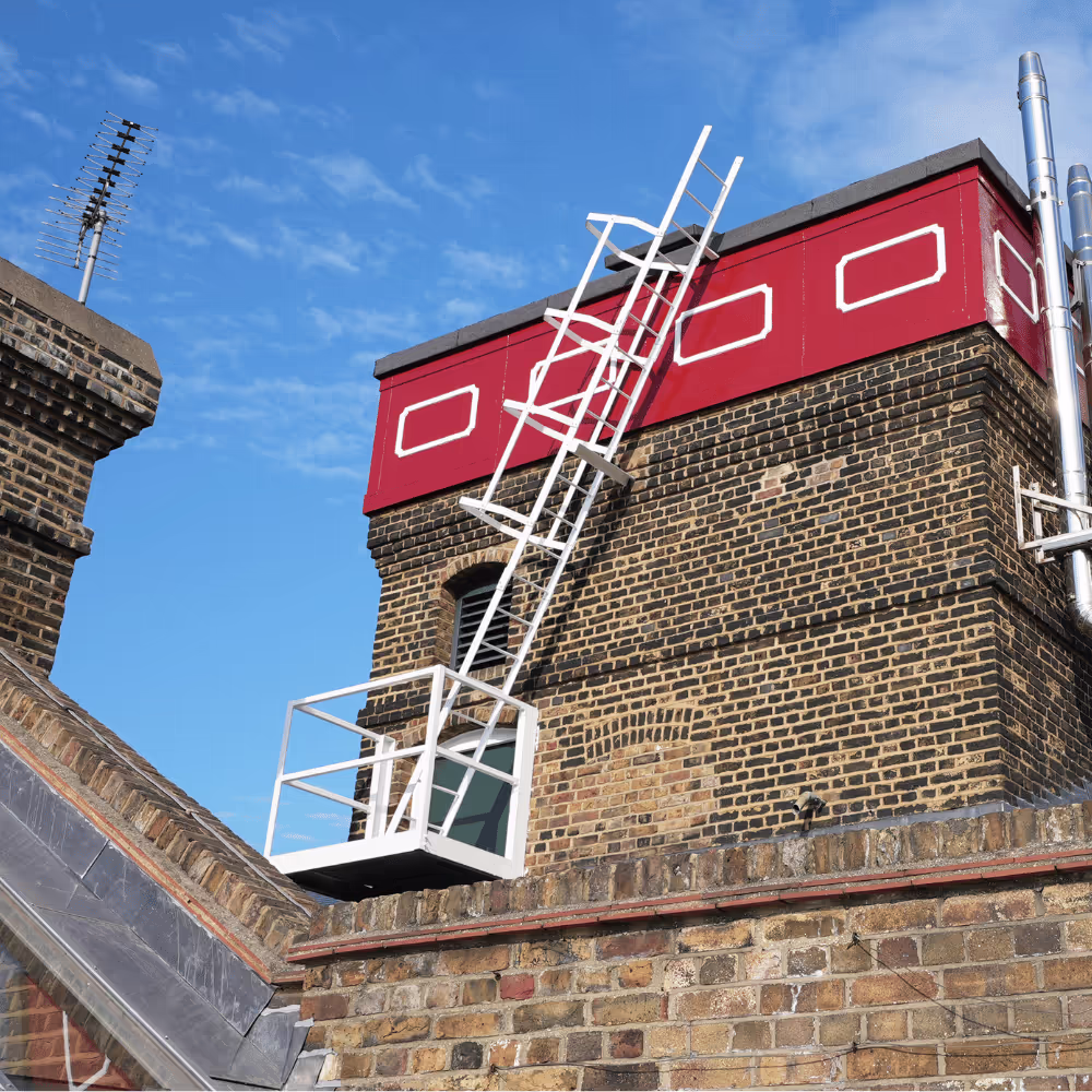 A newly installed white metal access ladder and gantry on the side of a historic brick and red-painted roof tower, part of a safety upgrade.