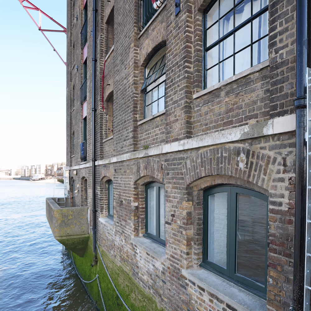 The historic brick facade of the Grade II listed Thames Tunnel Mills warehouse, showing the upgraded windows and masonry at the water's edge.