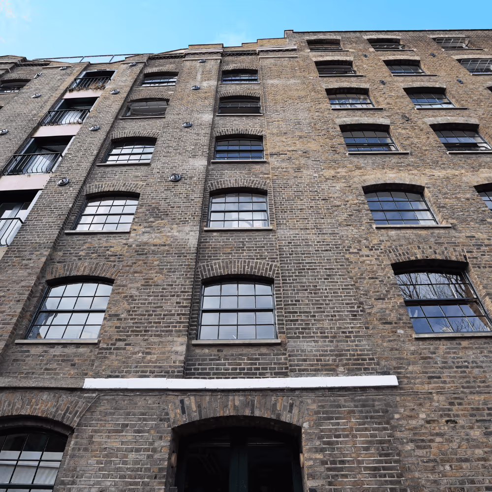 Low-angle view of the towering brick facade of the restored Grade II listed warehouse, showing the numerous, uniform arched windows.