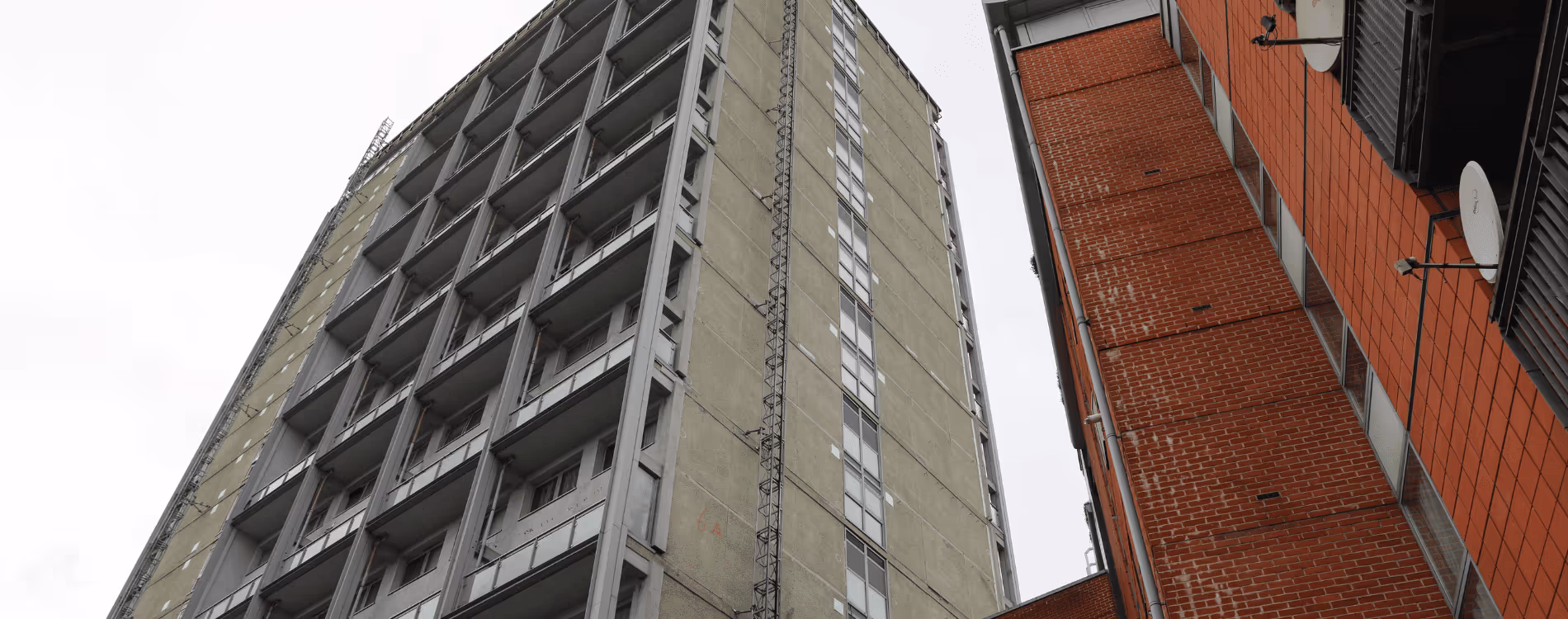 An upward-facing view contrasting two high-rise buildings in Westminster: a tall, older concrete or rendered tower block with fire escape ladders, and a newer or refurbished red brick building, illustrating the different structures covered by the Fire Risk Assessment (FRA) Programme.