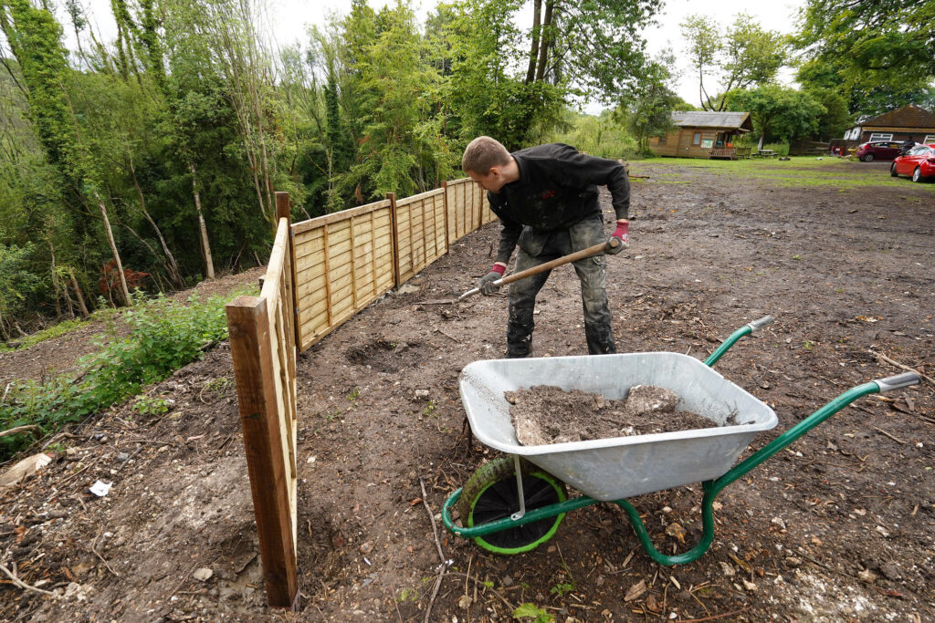 Team member preparing ground and installing fencing in a green outdoor setting to support biodiversity and habitat improvement.